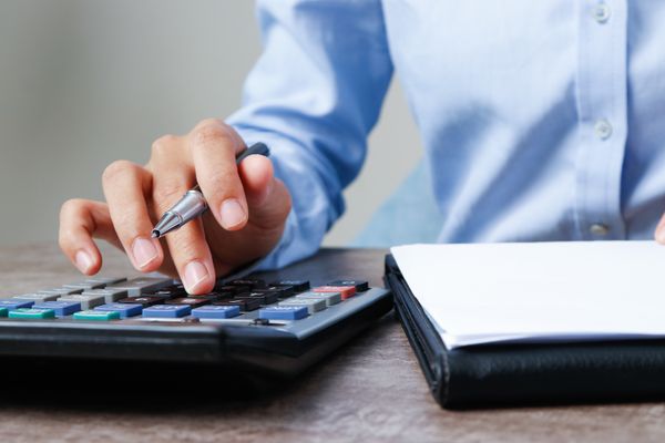 Man's hand holds a pen and works a calculator beside a portfolio folder.